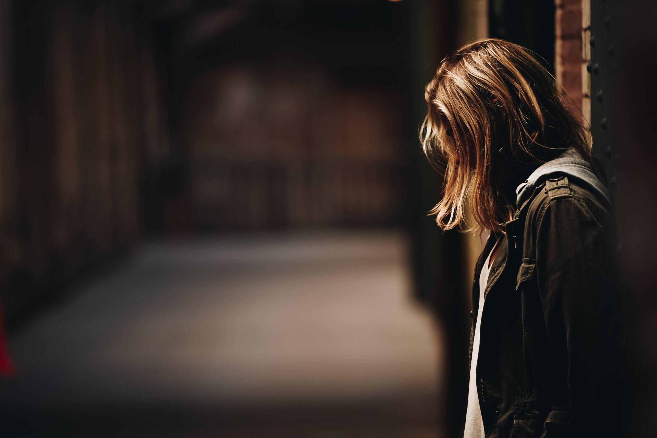 Profile shot of a woman leaning against a wall, head bowed