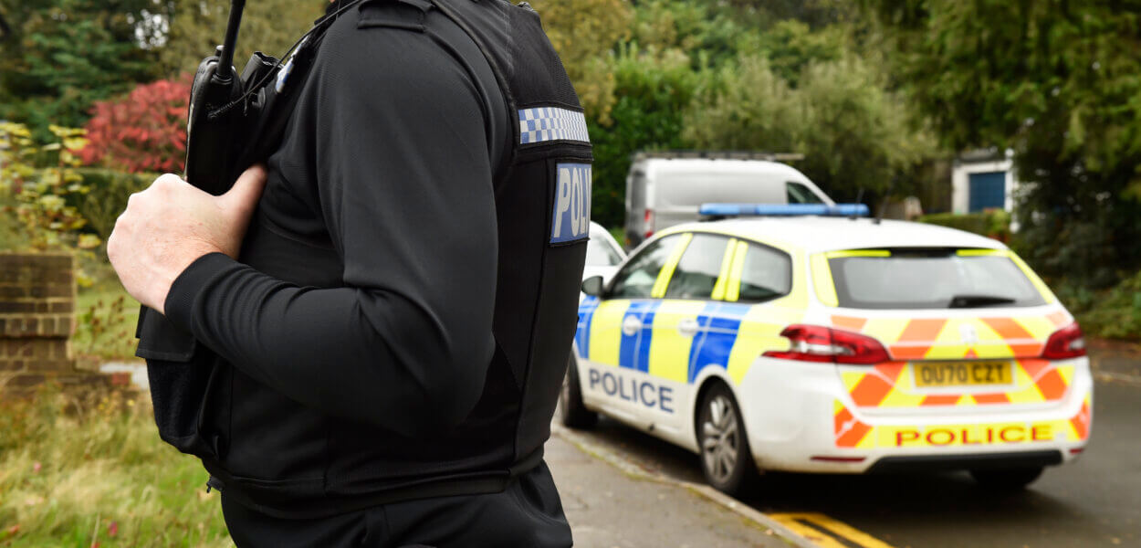 A Thames Valley police officer by a police vehicle in a village.